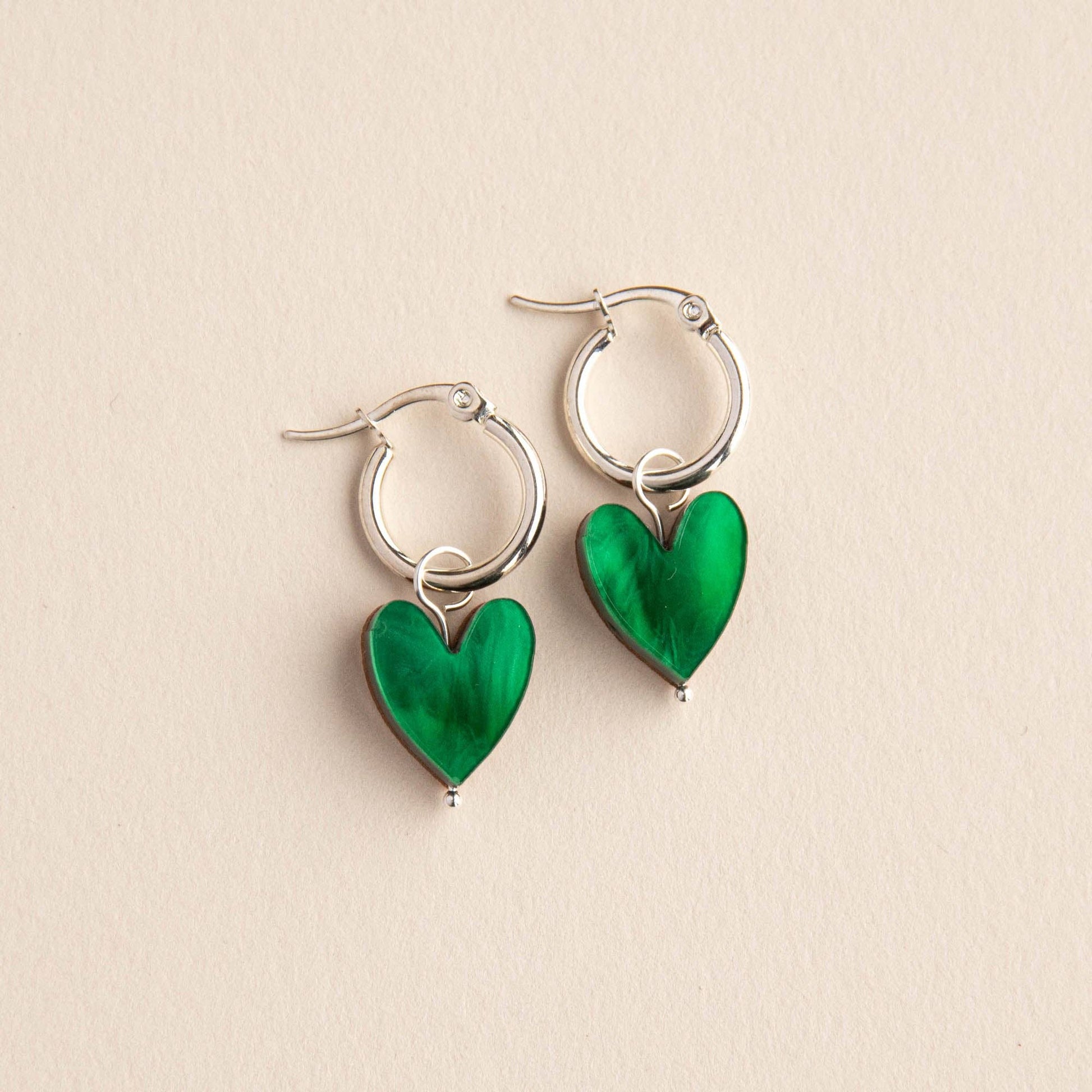Silver hoop earrings with green heart charms on a beige background