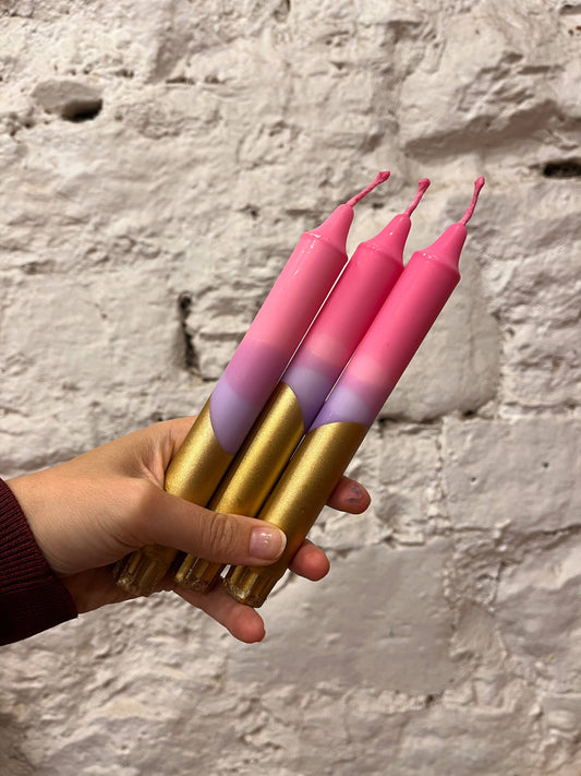 Hand holding pink and gold gradient candles against a stone wall background
