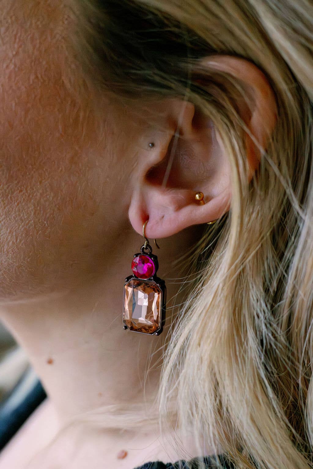 Close-up of an ear wearing a decorative earring with a pink gemstone.