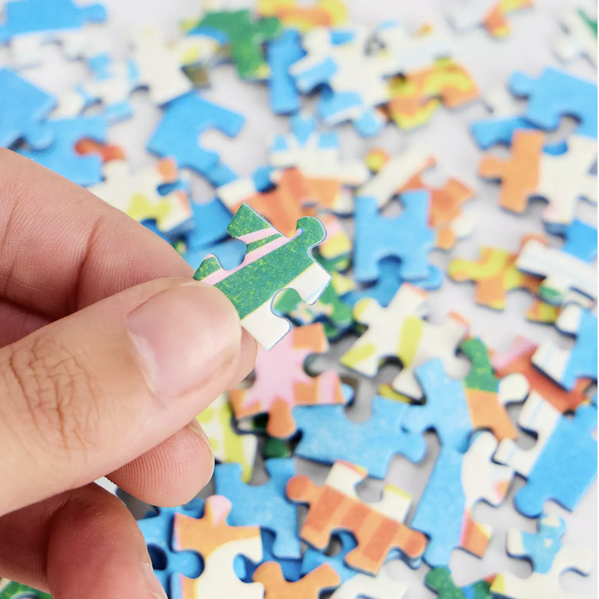 Hand holding a puzzle piece over a colorful jumble of puzzle pieces.
