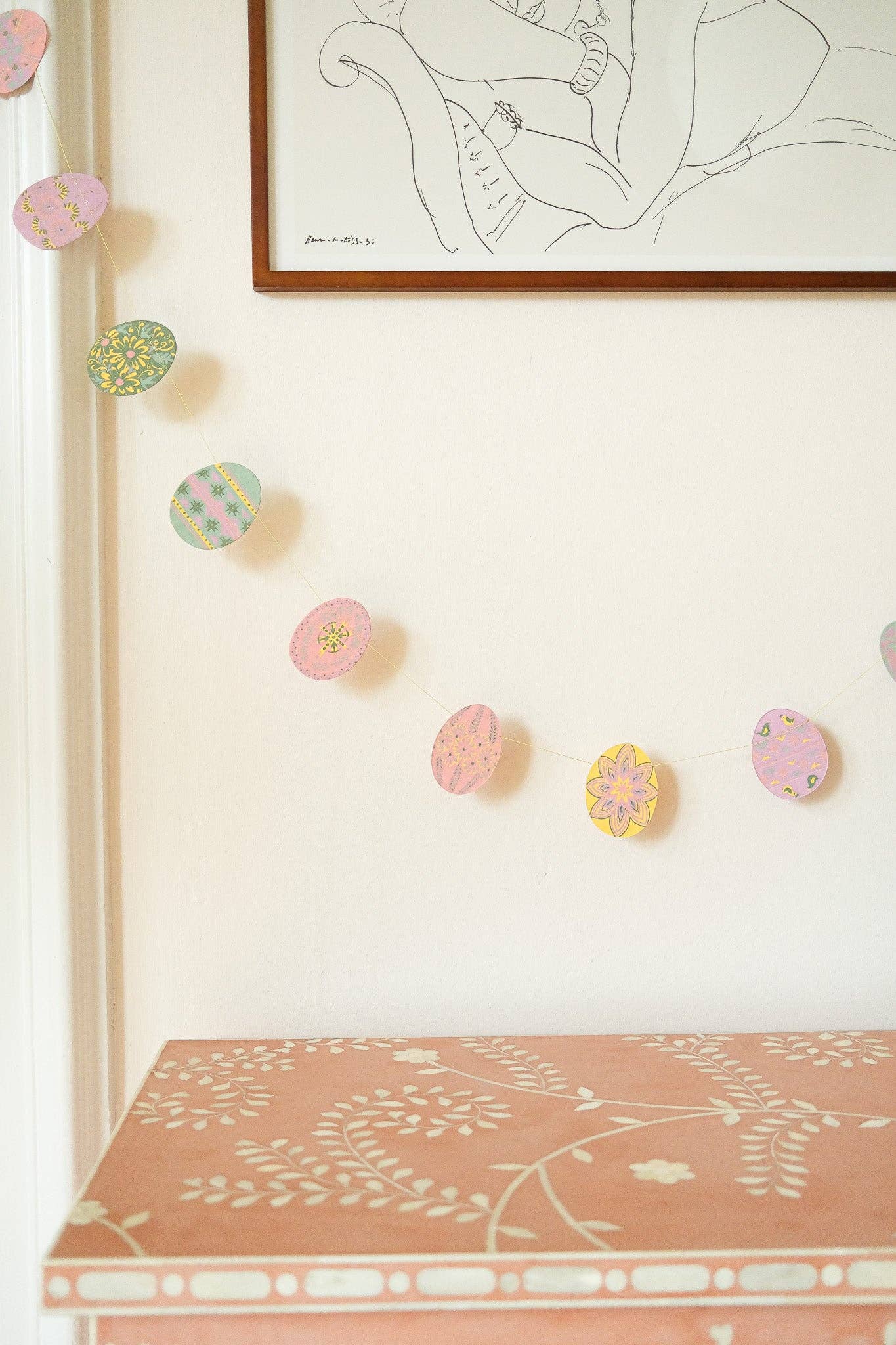 Decorative wall with colorful floral stickers and a framed artwork above a pink shelf.