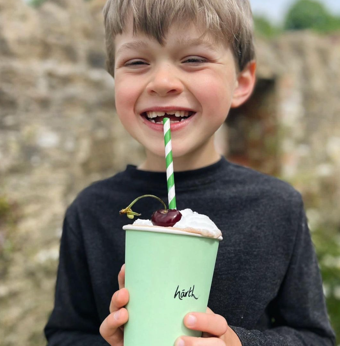 Child holding a green cup with a straw and cherry, outdoors.