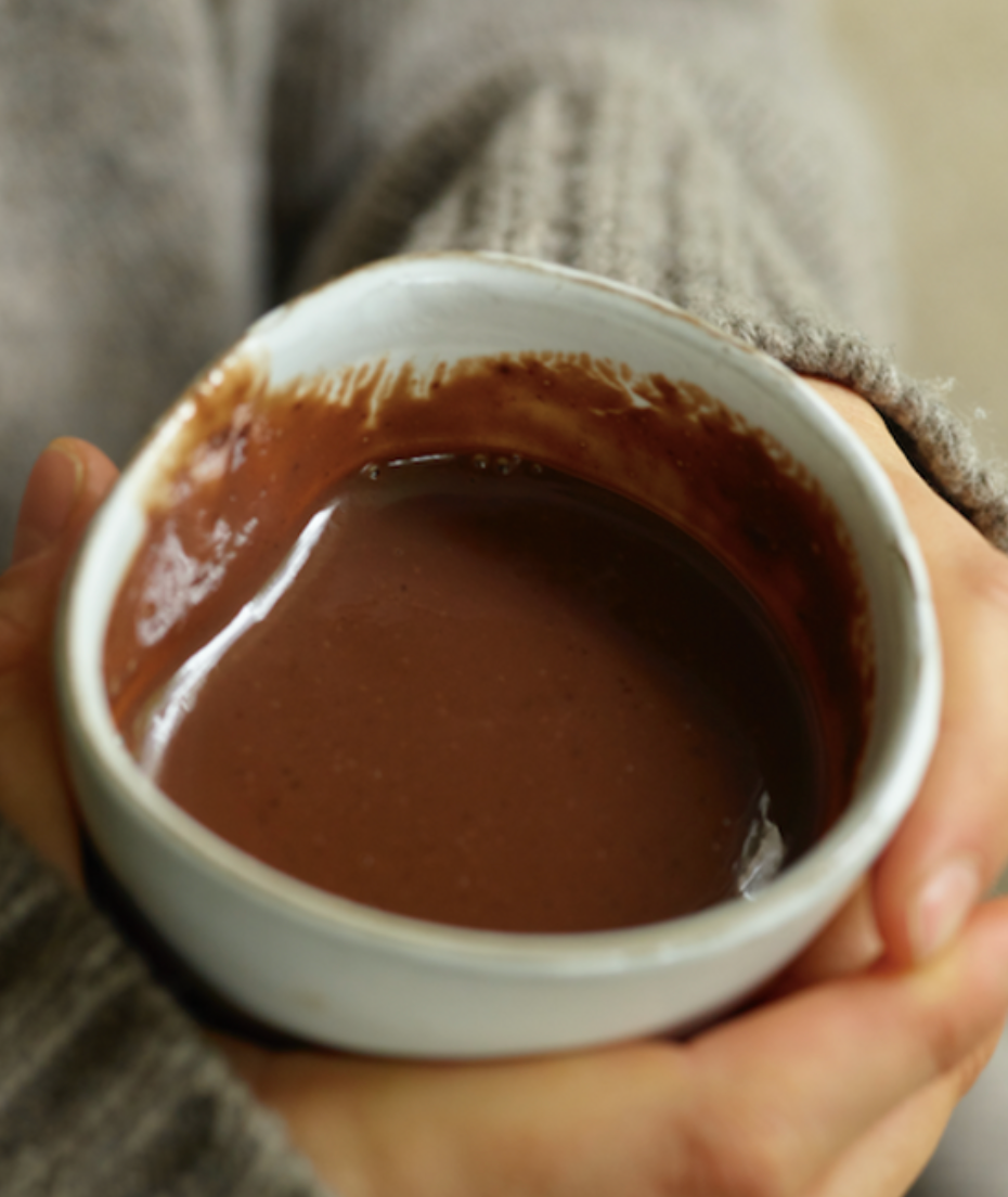 Person holding a small white bowl filled with a brown liquid, possibly hot chocolate.
