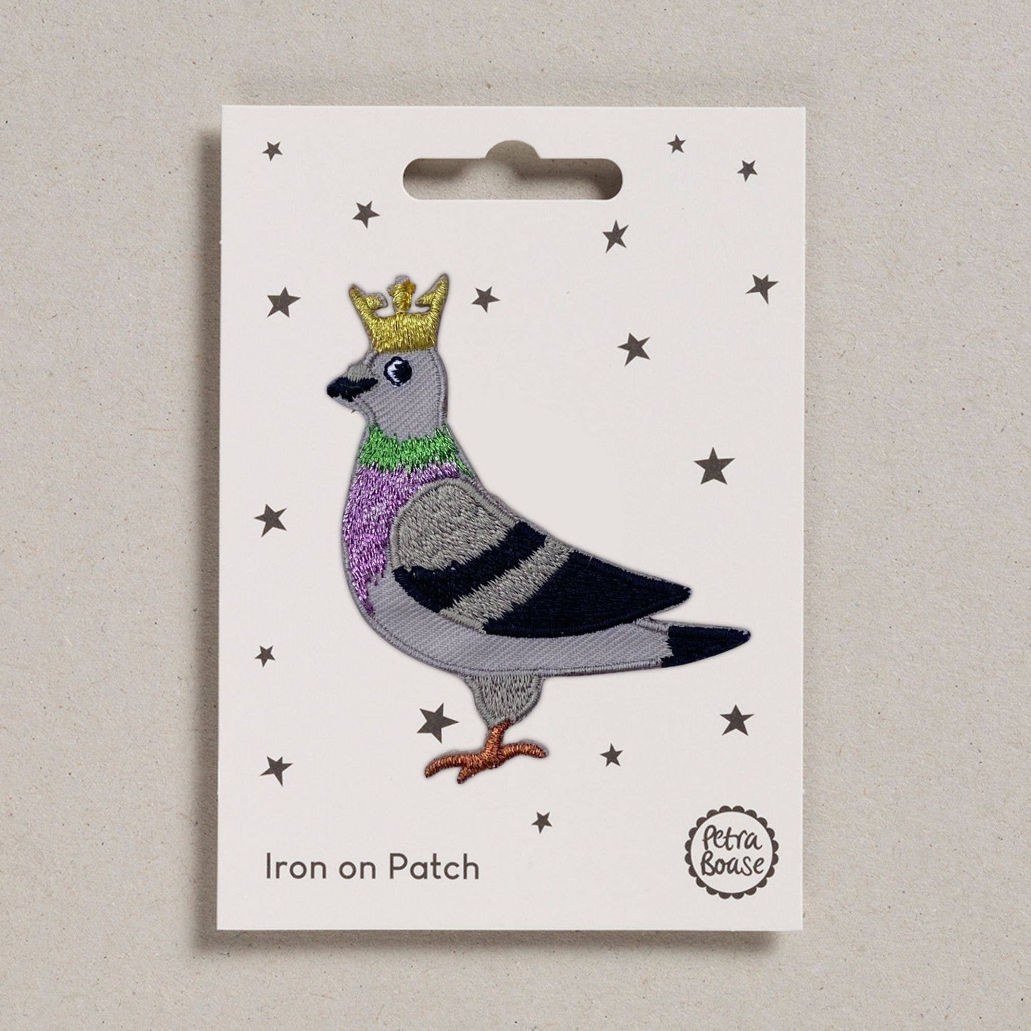 Iron on patch of a pigeon with a crown on a white card with star patterns, brand 'Petra Boase' visible.