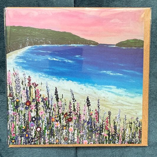A square card depicting a hand-painted beach scene with a soft-pink sky, with wildflowers in the foreground.