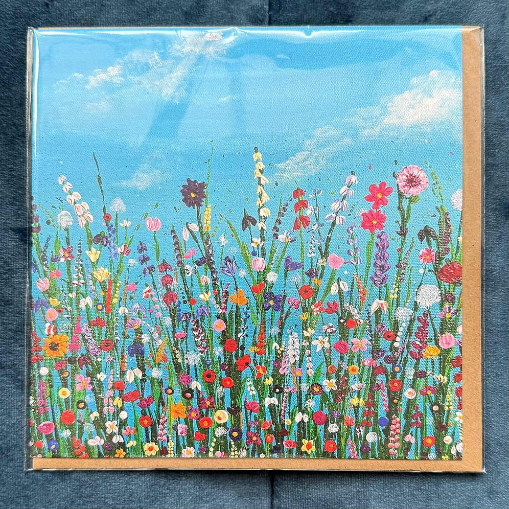 A square card of a vibrant wildflower meadow under a bright blue sky, displayed on a dark textured fabric background.