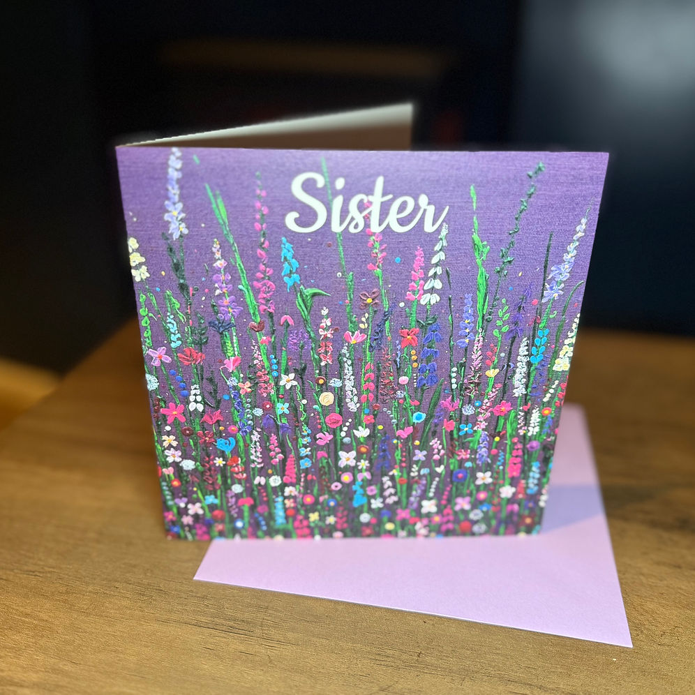 A square greeting card with a purple background and painted colourful wildflowers, printed with the word 'Sister' in white script on the top.