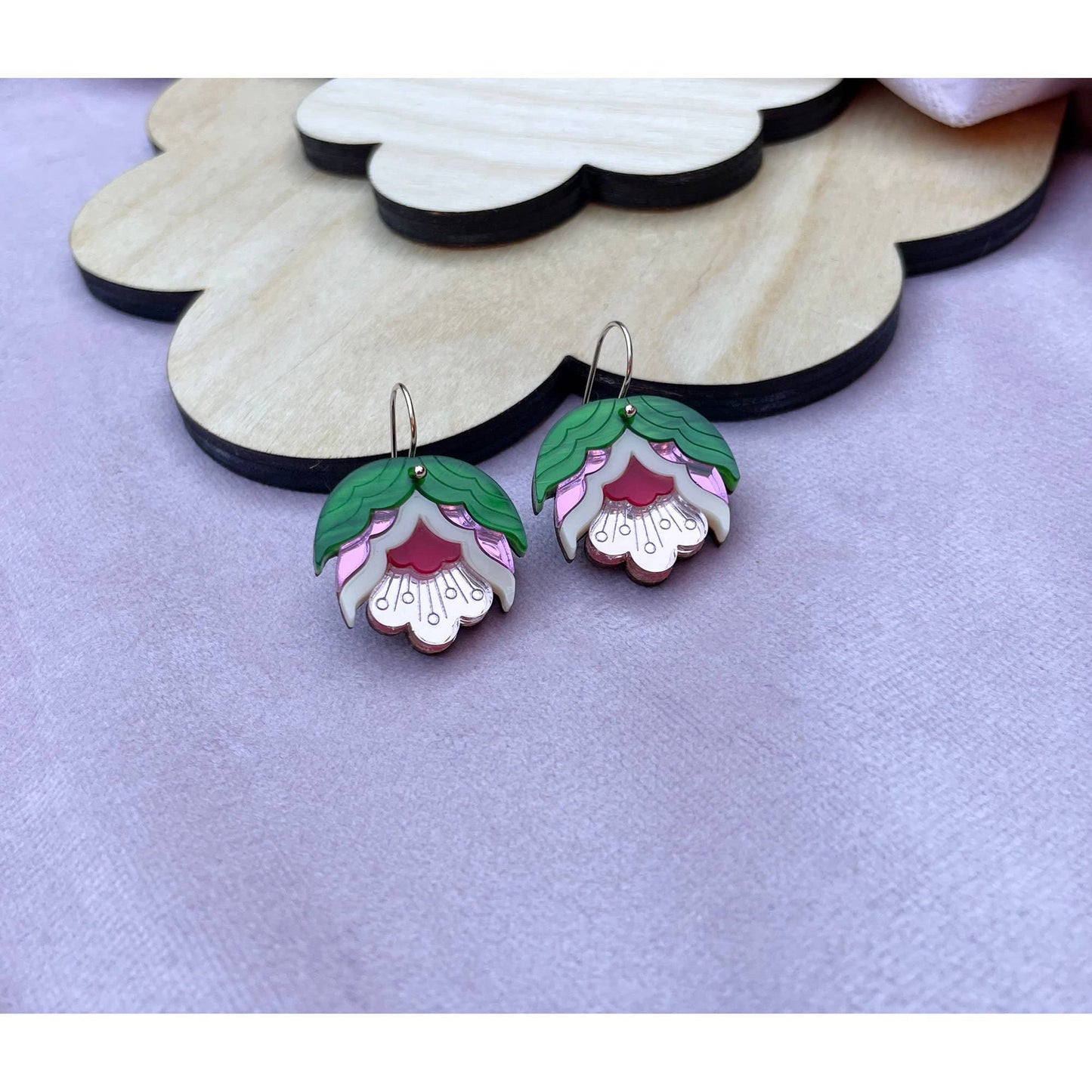 Floral earrings on a wooden stand with a purple background