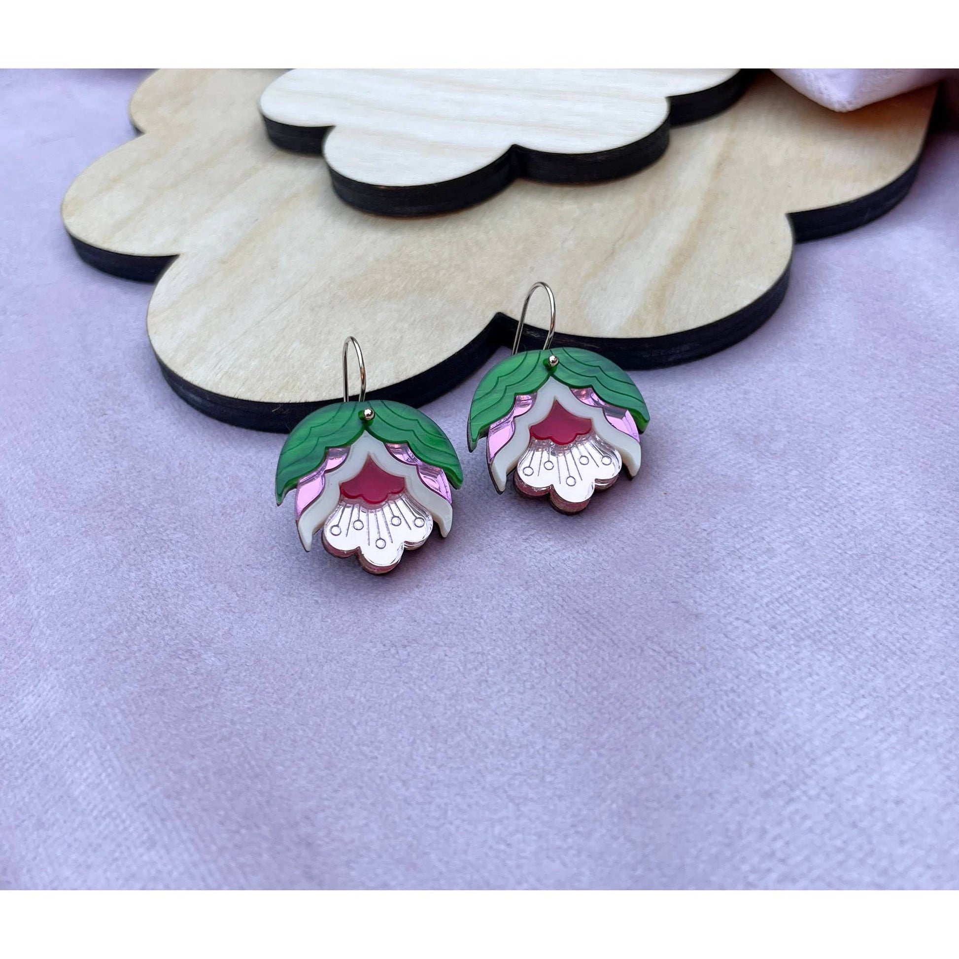 Floral earrings on a wooden stand with a purple background