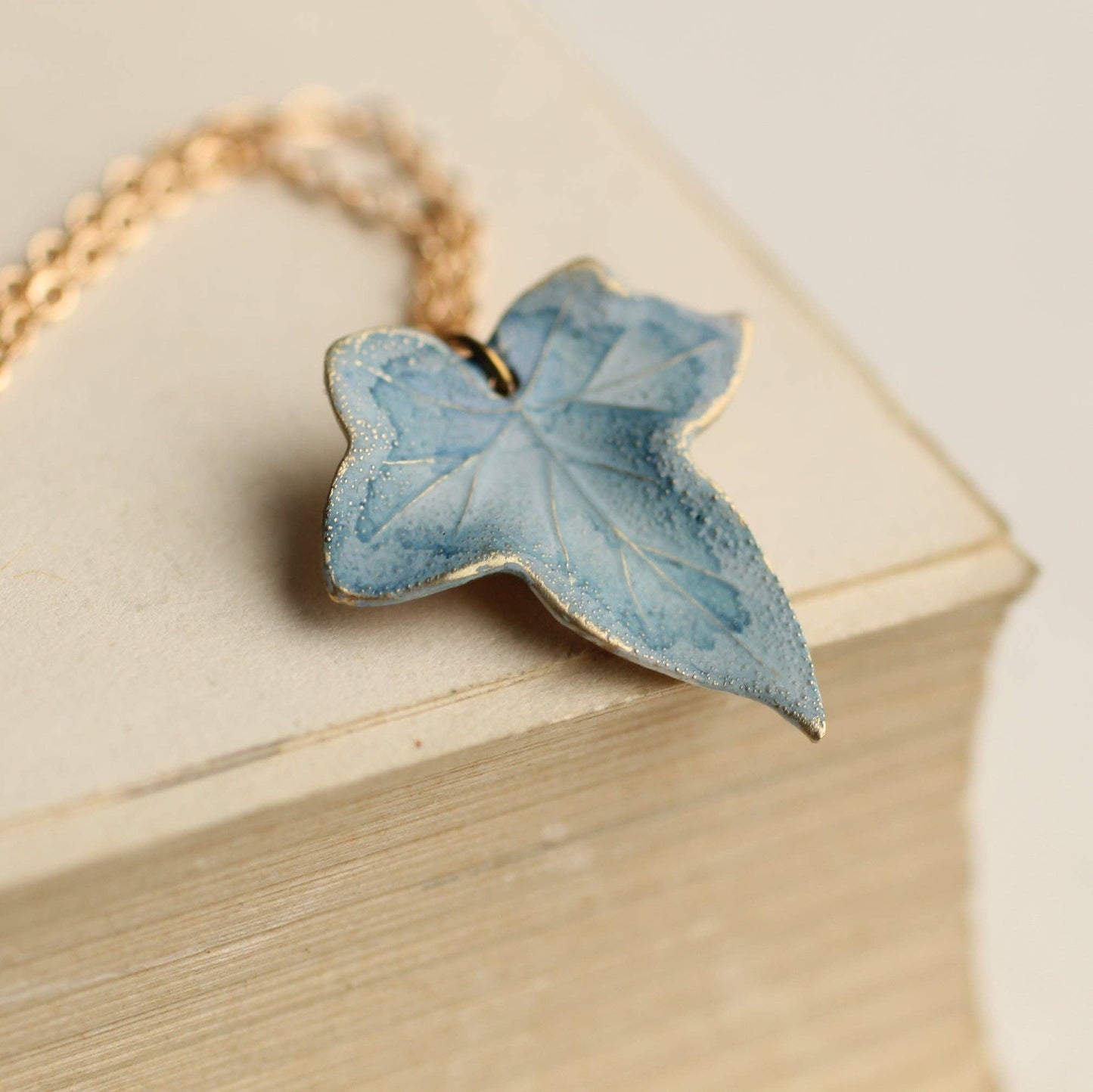 Blue butterfly-shaped pendant on a gold chain against a beige background