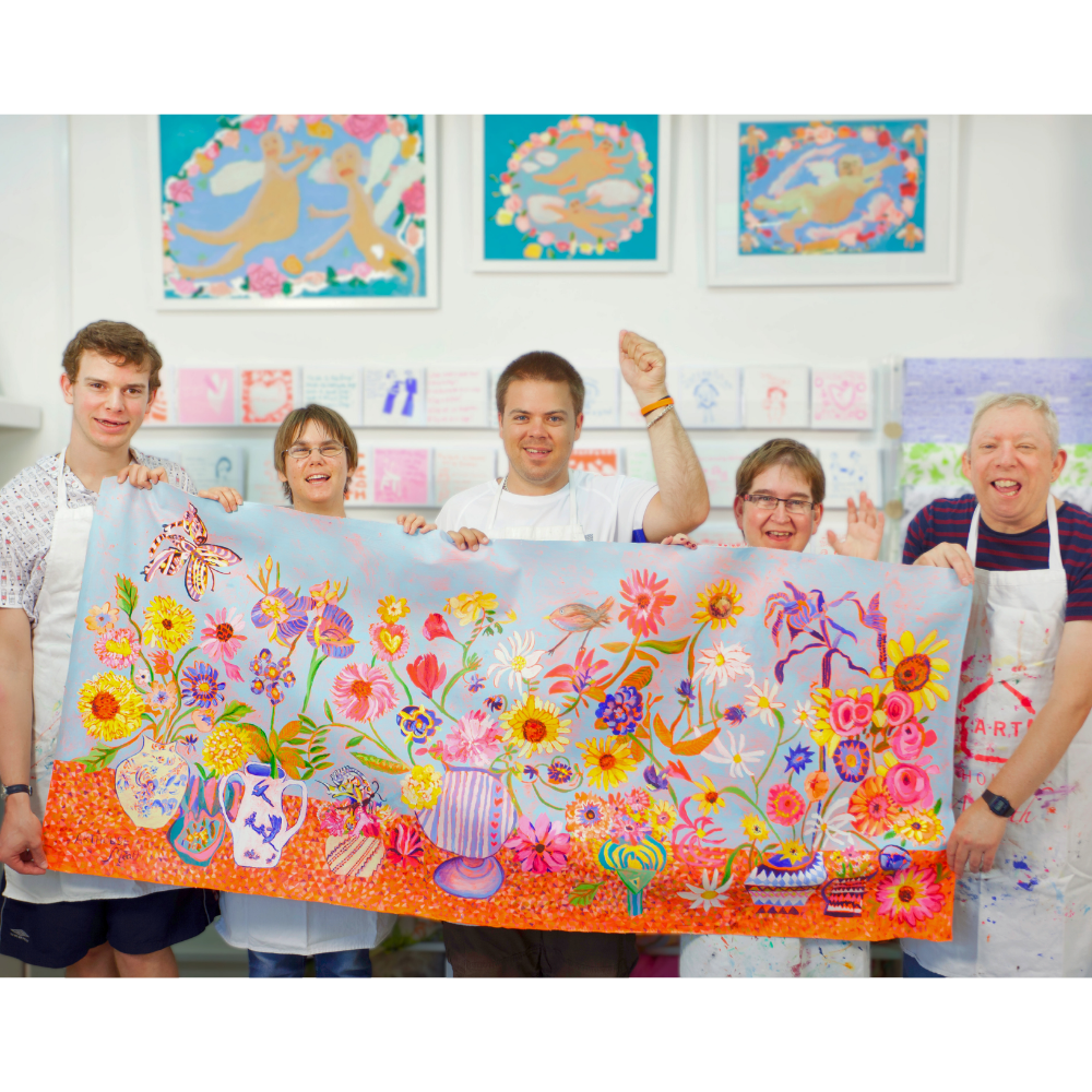 Group of people holding a colorful floral artwork in an art studio.