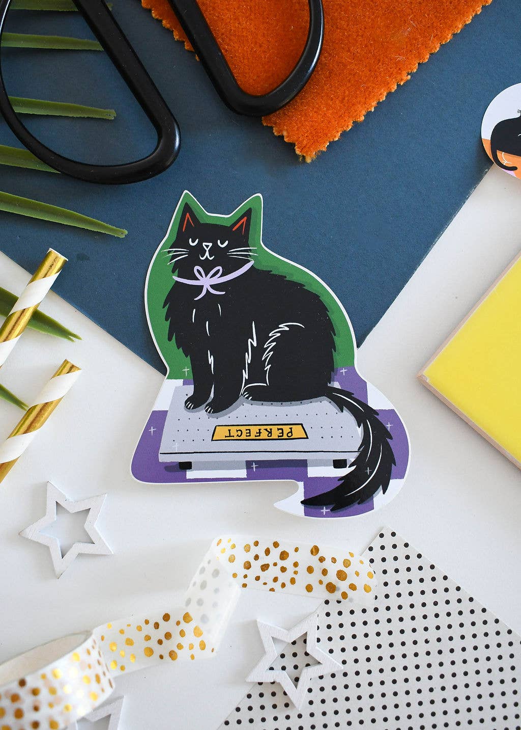 Decorative sticker of a black cat on a scale with stationery items on a colorful background