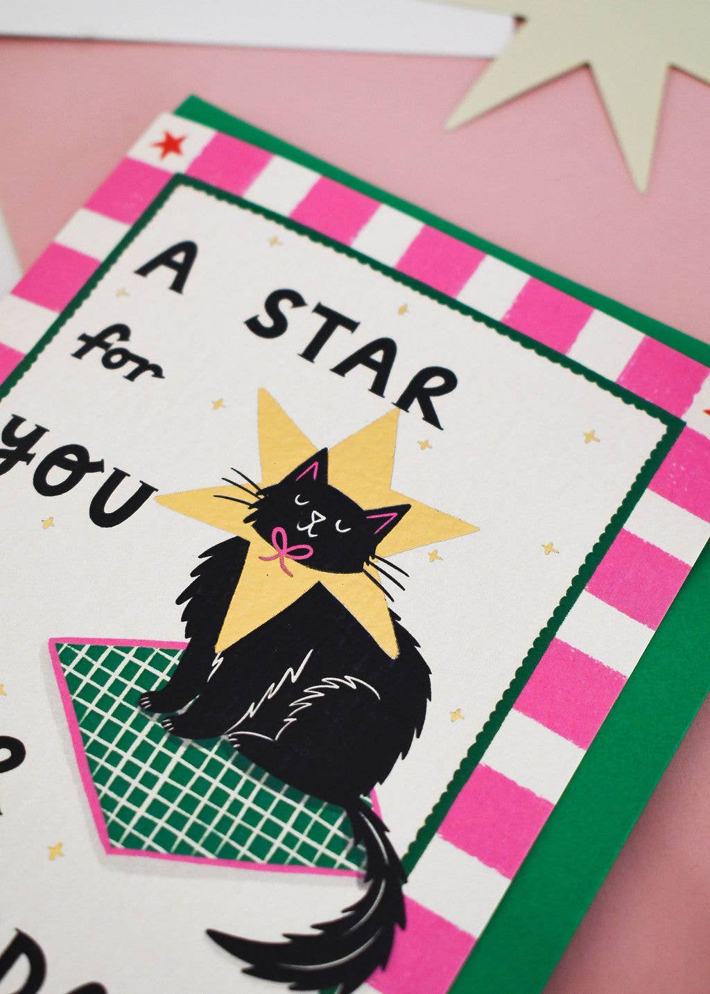 A close-up of a handmade greeting card featuring a black cat sitting inside a yellow star, with pink and green striped borders and the text 'A STAR for YOU'.
