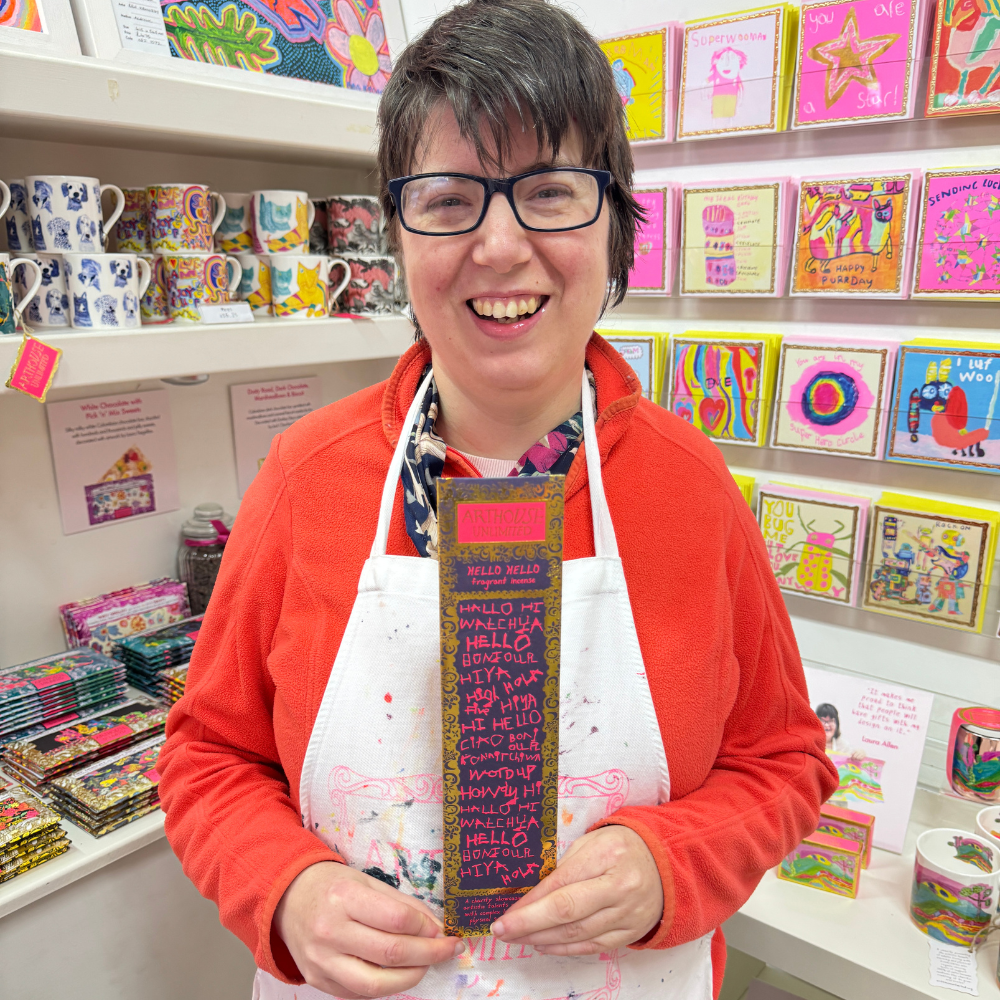 Person holding a colorful scarf in a store with greeting cards and mugs on shelves.