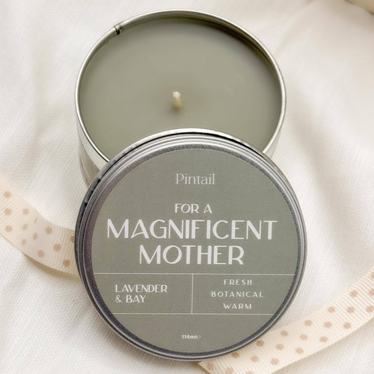 Candle in a tin labeled 'For a Magnificent Mother' by Pintail on a light fabric background.