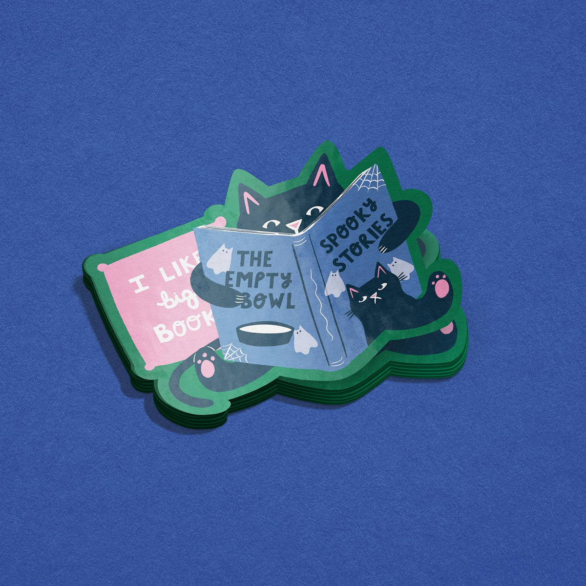 A stack of illustrated die-cut stickers featuring a black cat reading spooky books, shown on a textured blue background. The visible sticker designs include a pink book reading 'I LIKE BOOES' and a blue book reading 'THE EMPTY BOWL' and 'SPOOKY STORIES'.