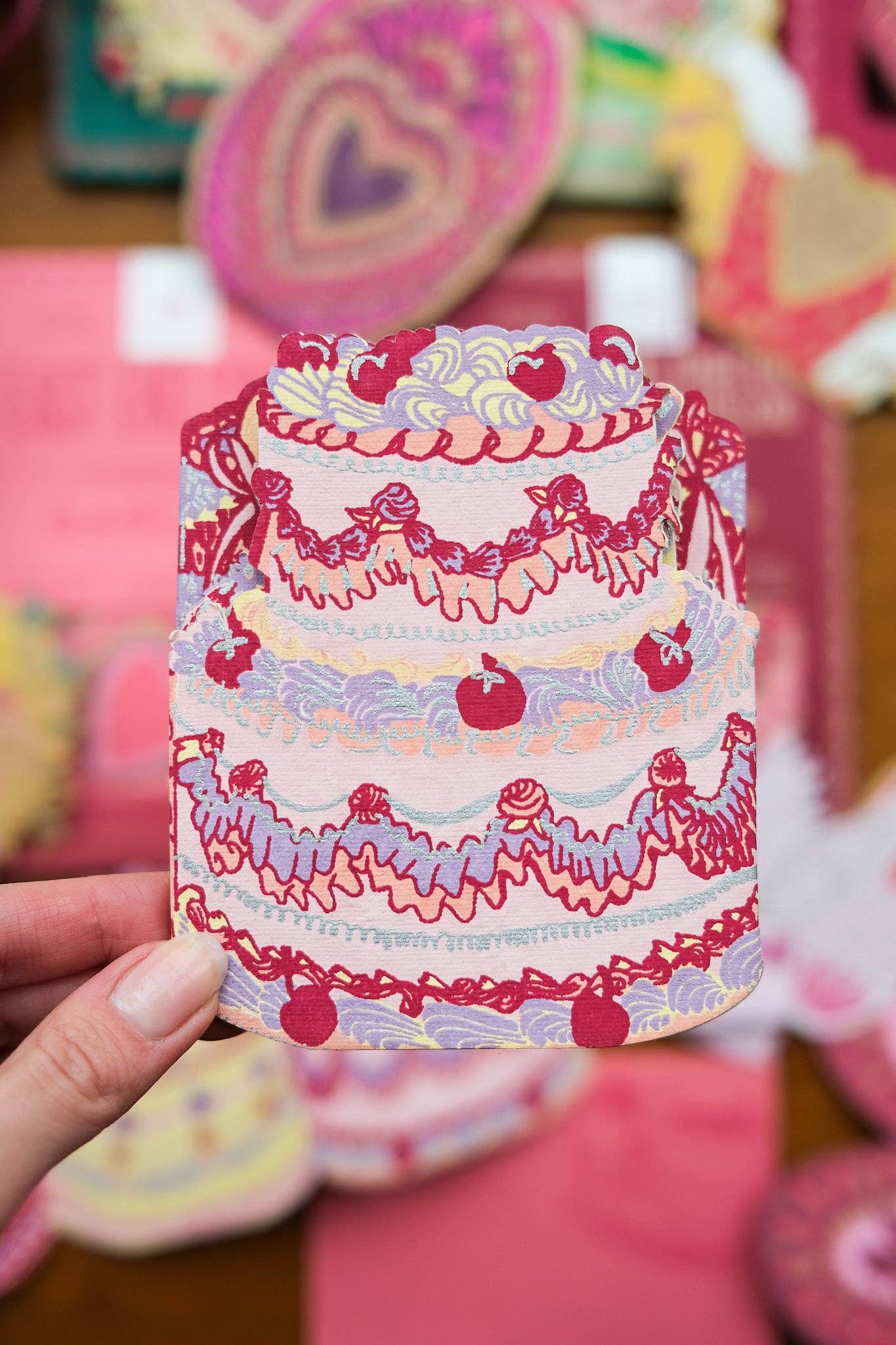 Colorful paper cake with decorative elements held by a hand against a blurred background