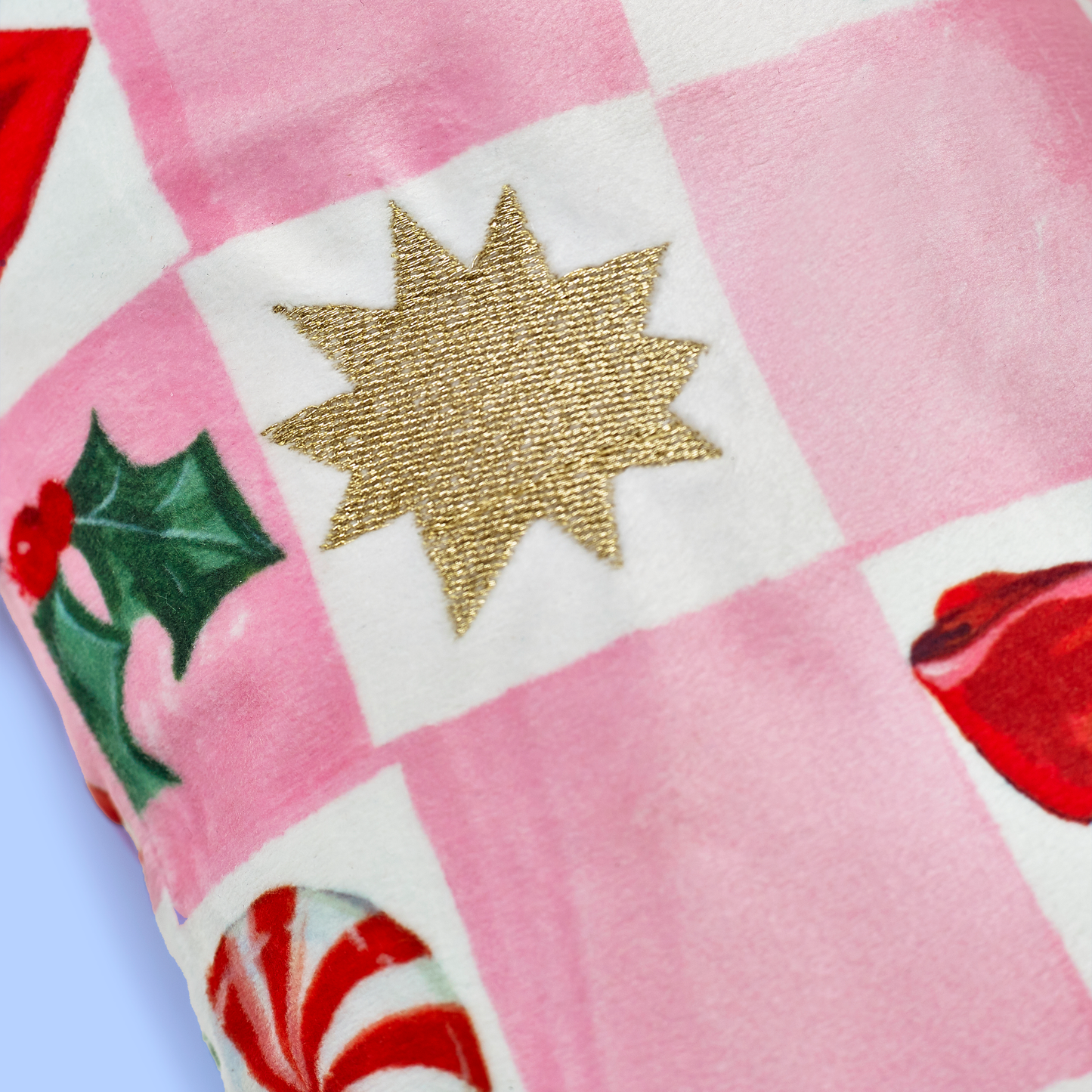 Close-up of a pink patchwork fabric with a gold star, holly leaf, peppermint candy, and red heart.