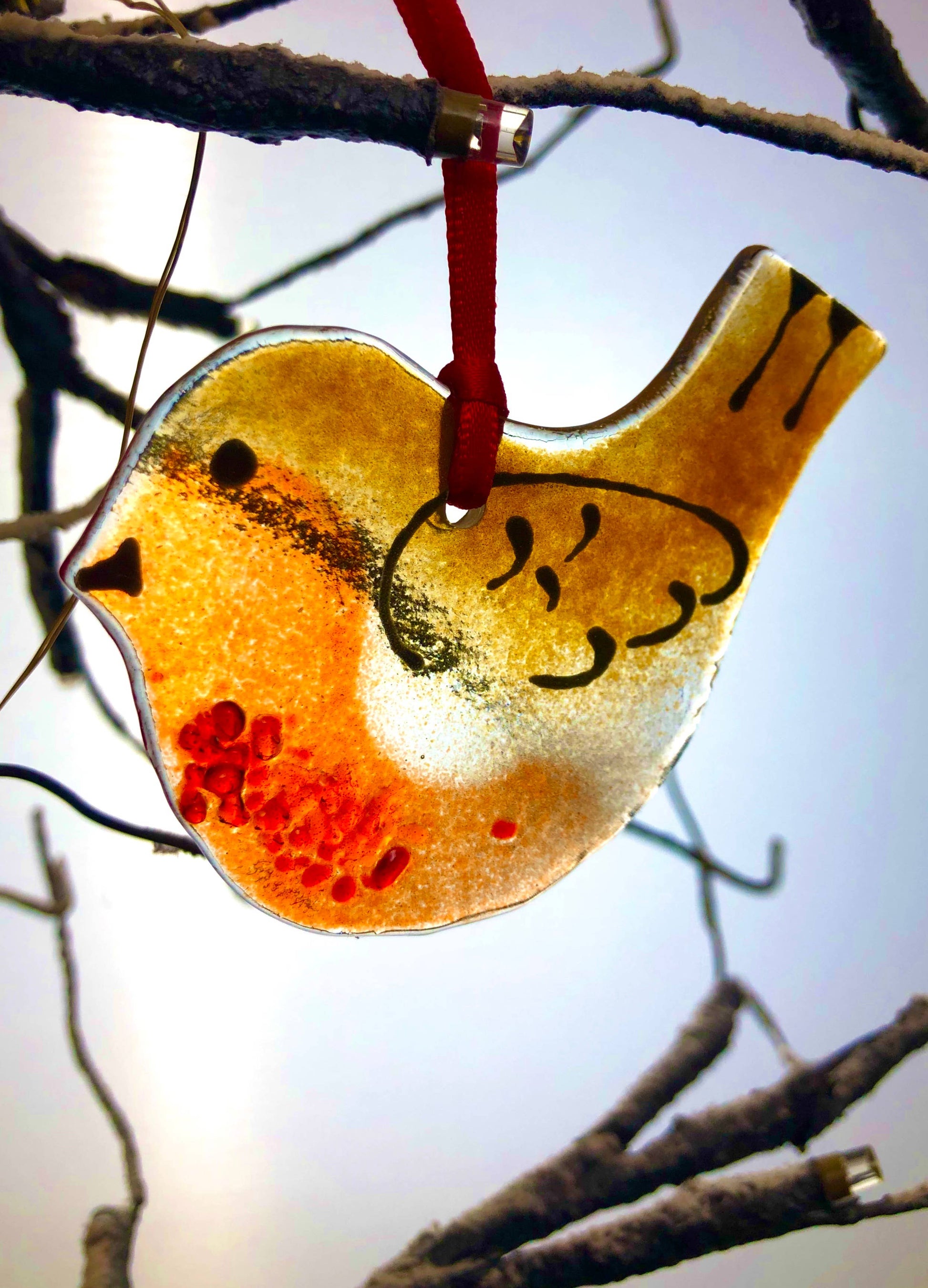 Decorative glass bird ornament hanging from a branch against a blurred natural background