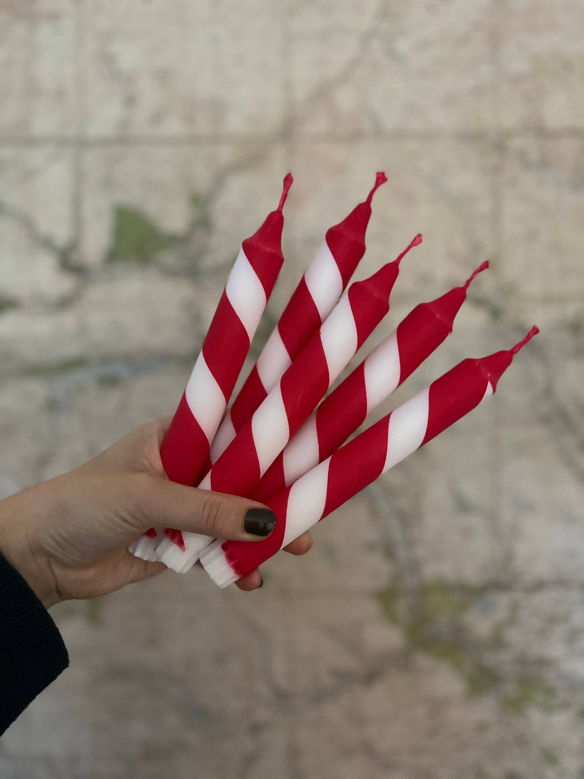 Hand holding red and white striped candles against a blurred background