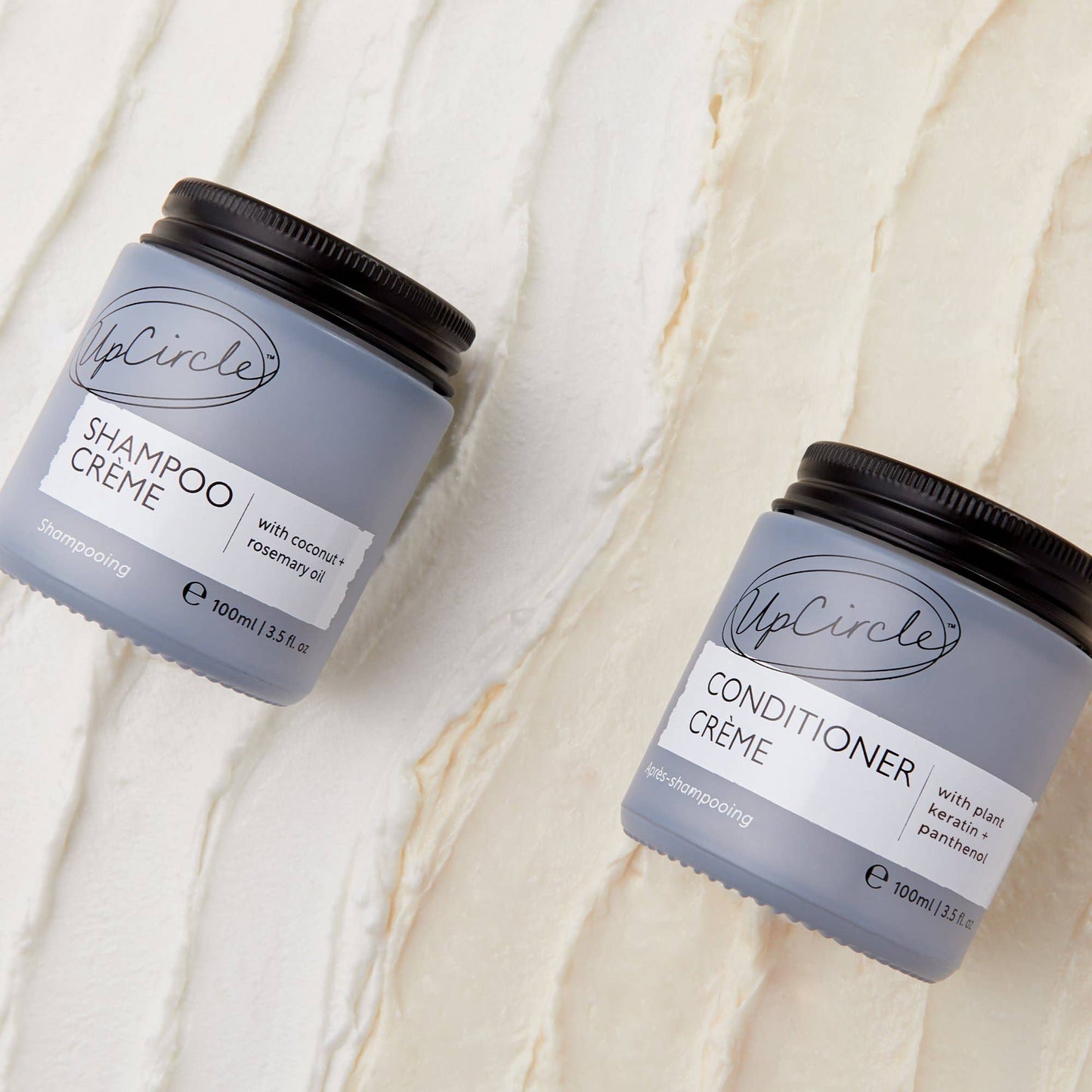 UpCircle Shampoo Crème and Conditioner Crème jars on a textured beige background
