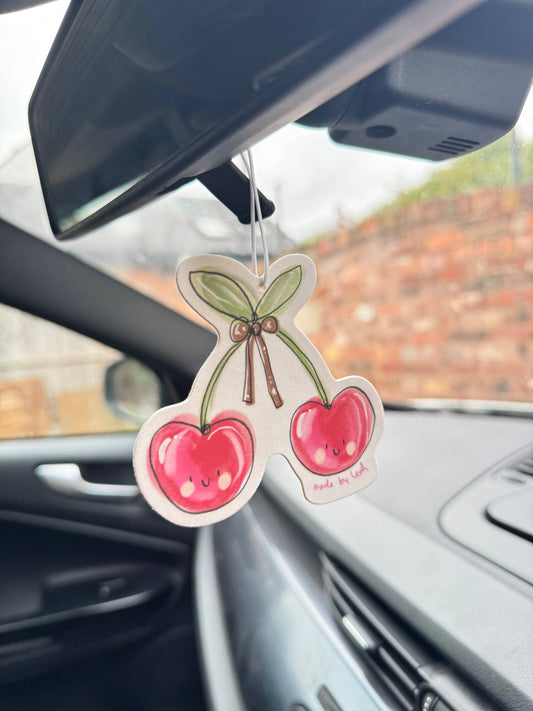 Car air freshener shaped like cherries hanging from a car's rearview mirror.