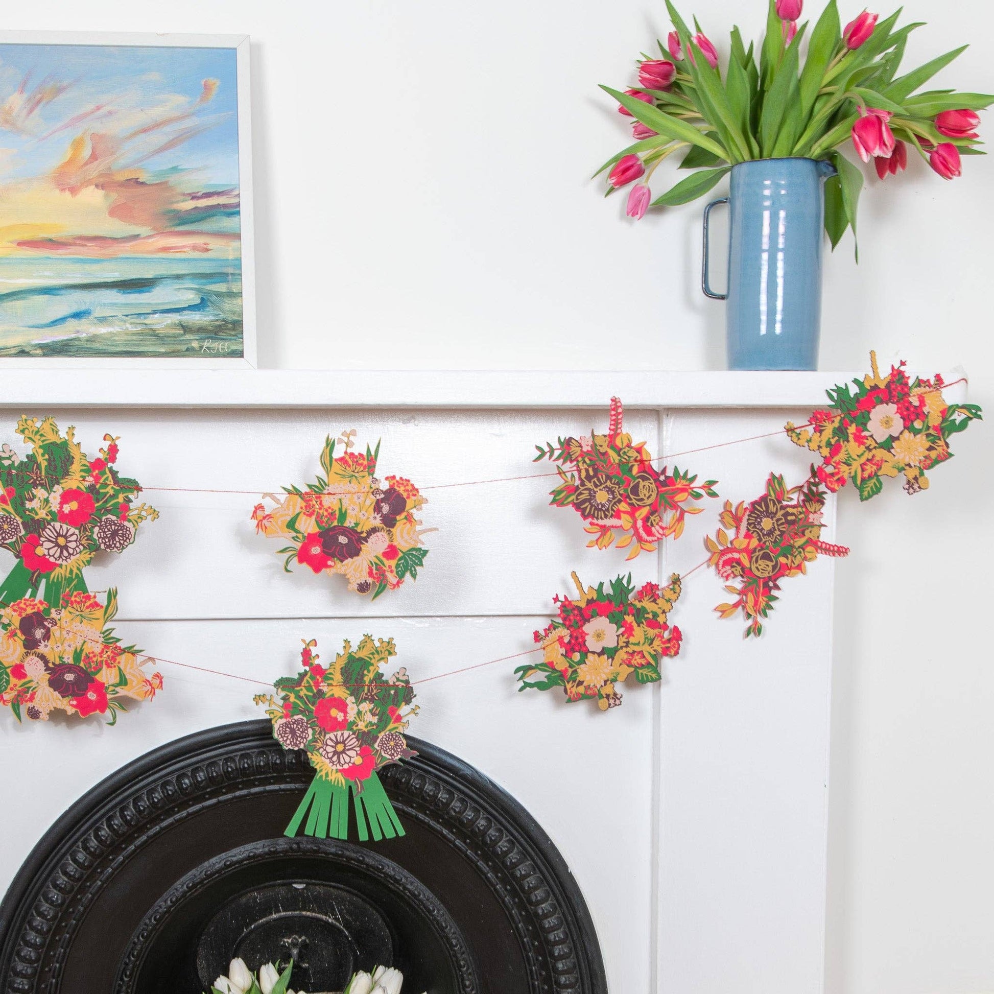 Decorative floral garland on a white wall with a vase of flowers and a painting.