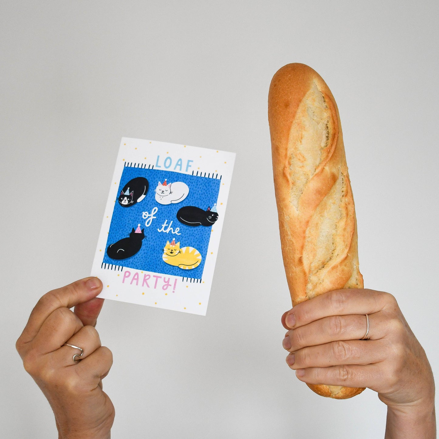 Person holding a loaf of bread and a card with cartoon characters on a plain background