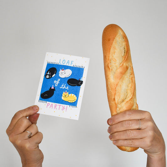 Person holding a loaf of bread and a card with cartoon characters on a plain background