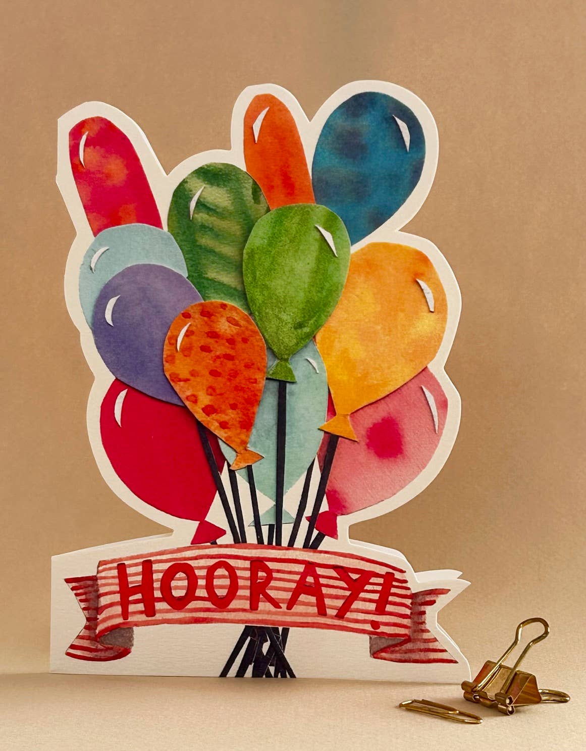 Colorful balloons with 'HOORAY!' banner on a beige background