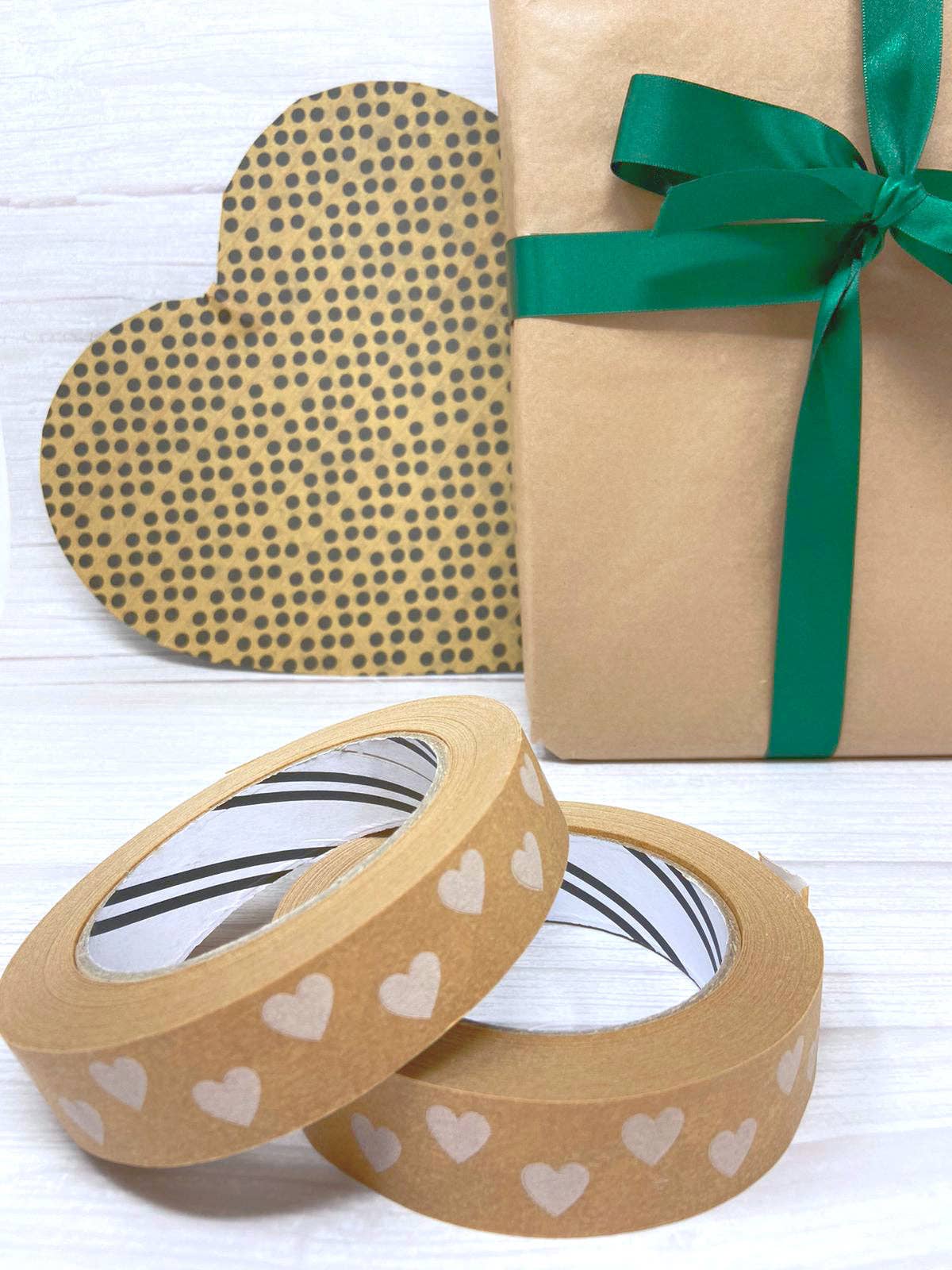 Two rolls of brown paper tape with heart patterns and a wrapped gift with a green ribbon on a white background.