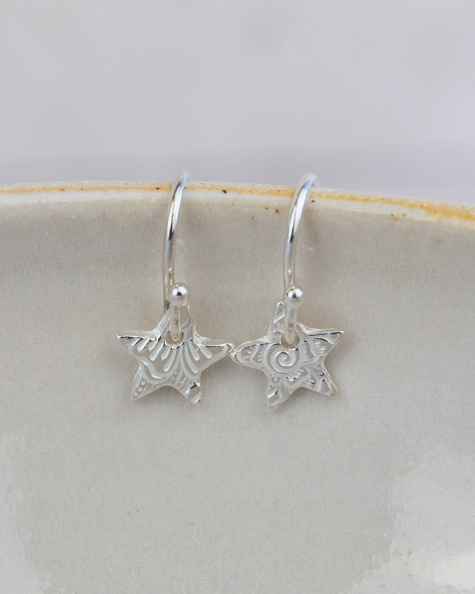 Silver star-shaped earrings on a white ceramic plate