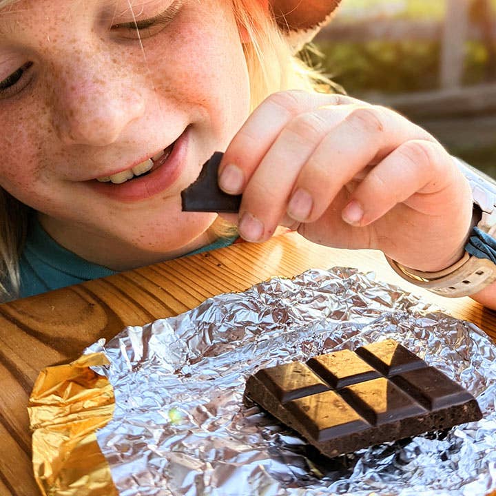 Child eating a chocolate bar with a piece of foil on a wooden surface