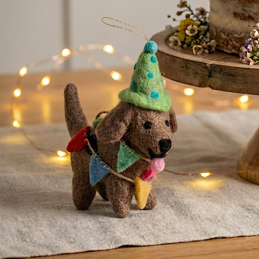 Felted dog ornament with a party hat on a textured surface with blurred lights in the background
