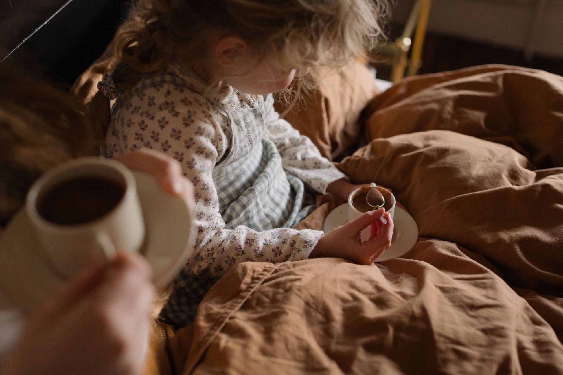 Child holding a cup of coffee next to an adult in bed