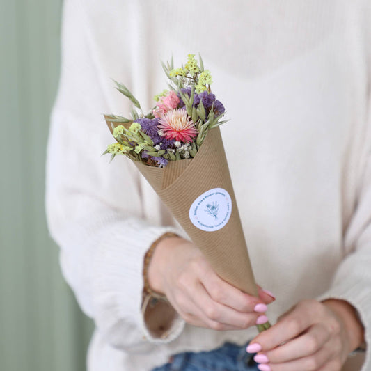 Bouquet of flowers wrapped in brown paper held by a person with a blurred background