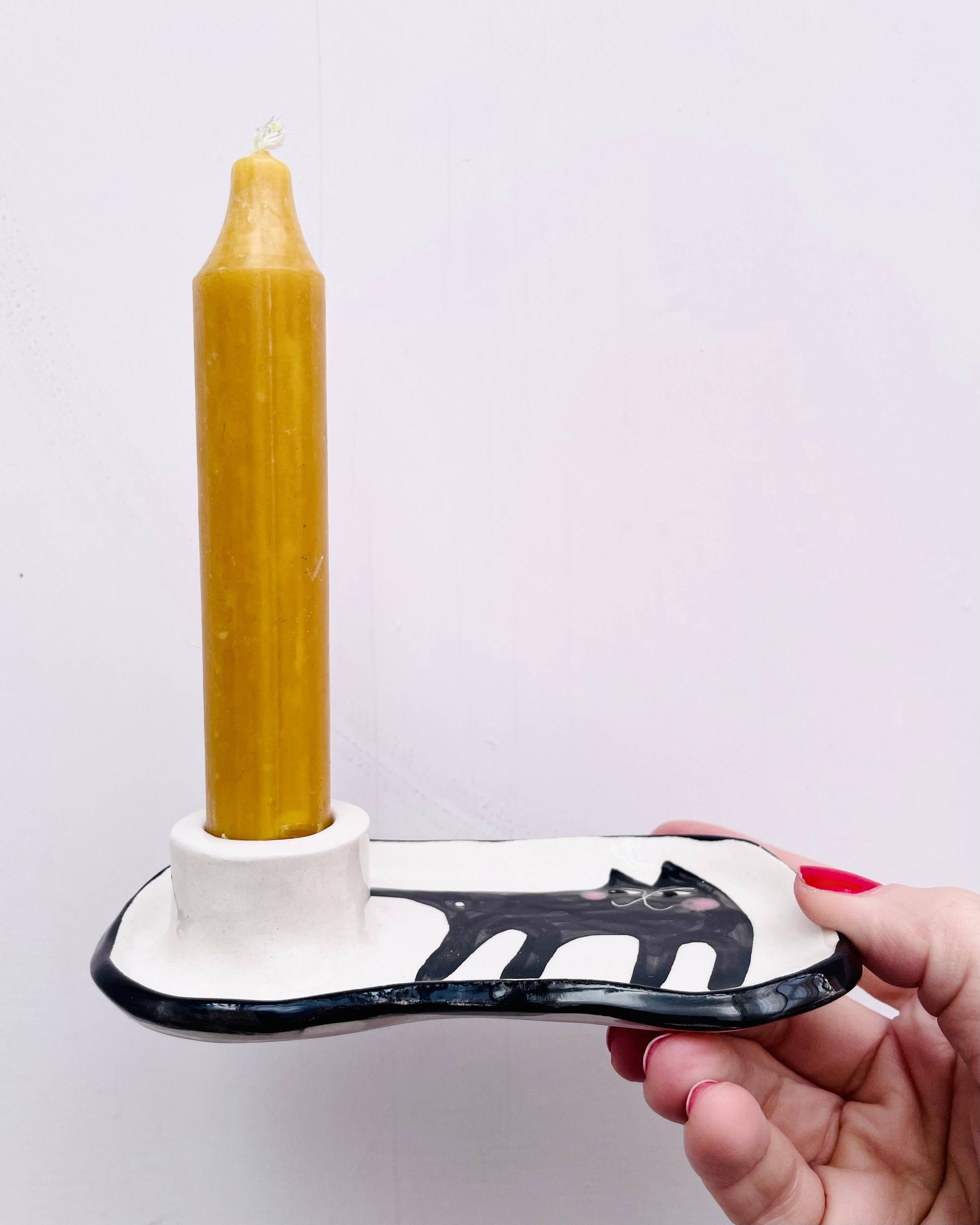Hand holding a white and black tool with a yellow candle on a white background