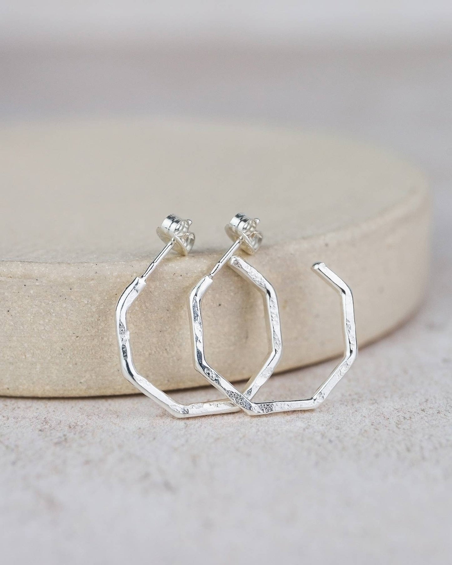 Silver geometric hoop earrings on a neutral background