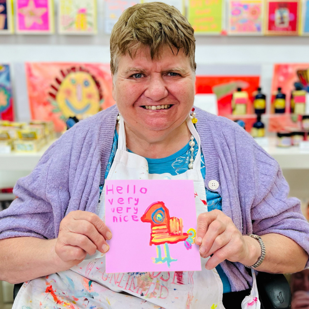 Person holding a colorful card with 'Hello very very nice' text in an art classroom setting.