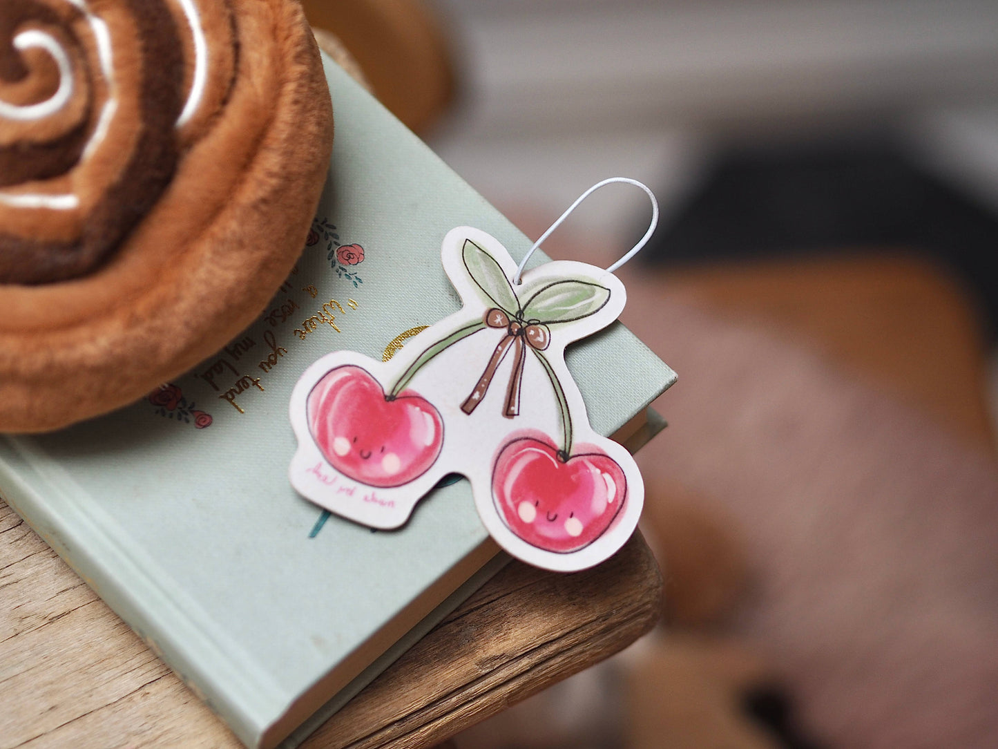 Sticker with cherry design on a book next to a cinnamon roll