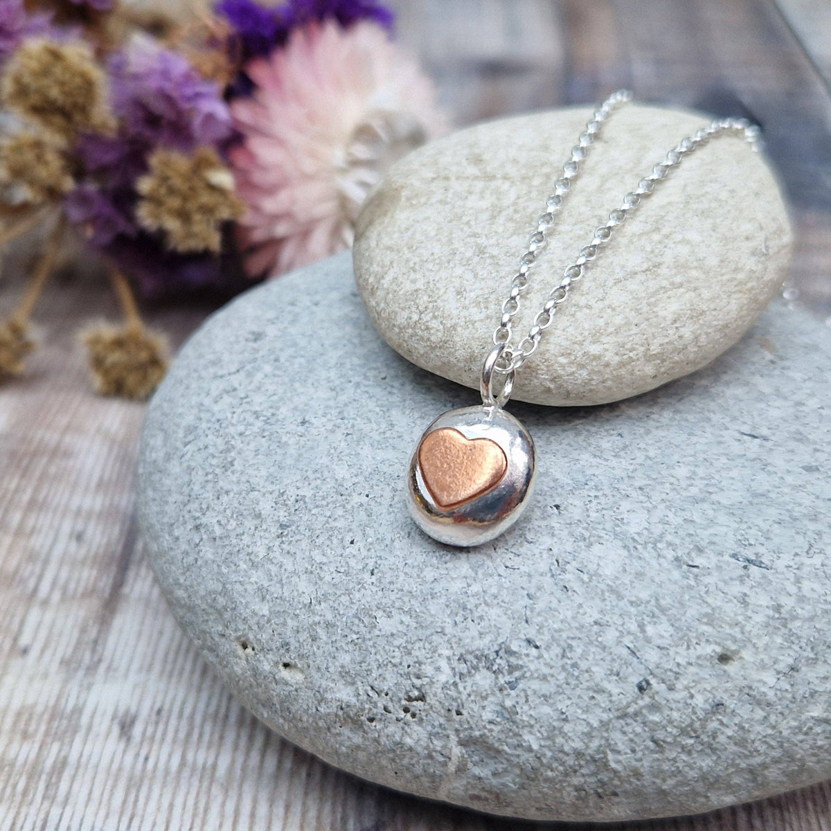 Necklace with a heart-shaped pendant on a stone surface with dried flowers in the background