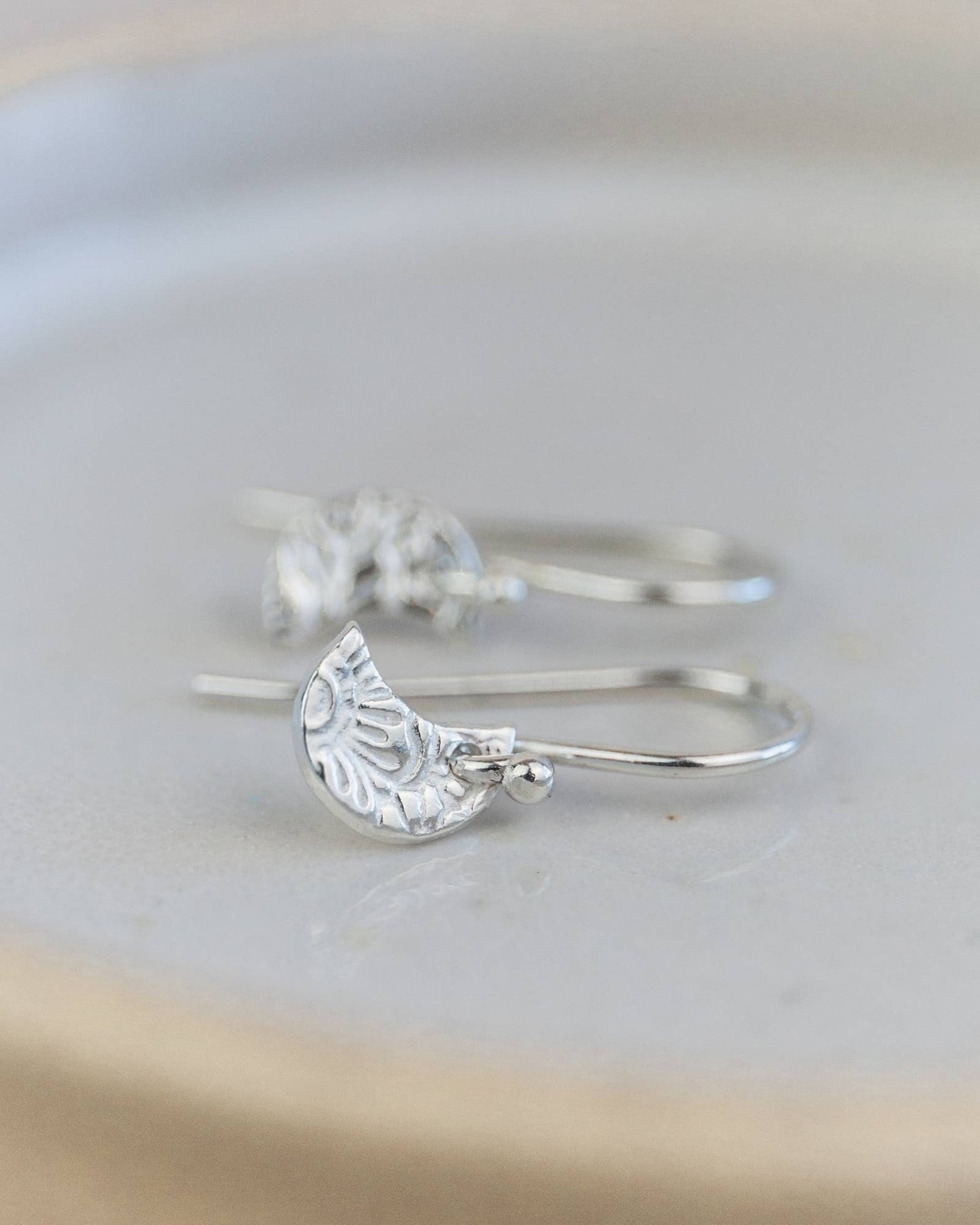 Silver earrings with half-circle designs on a light gray background