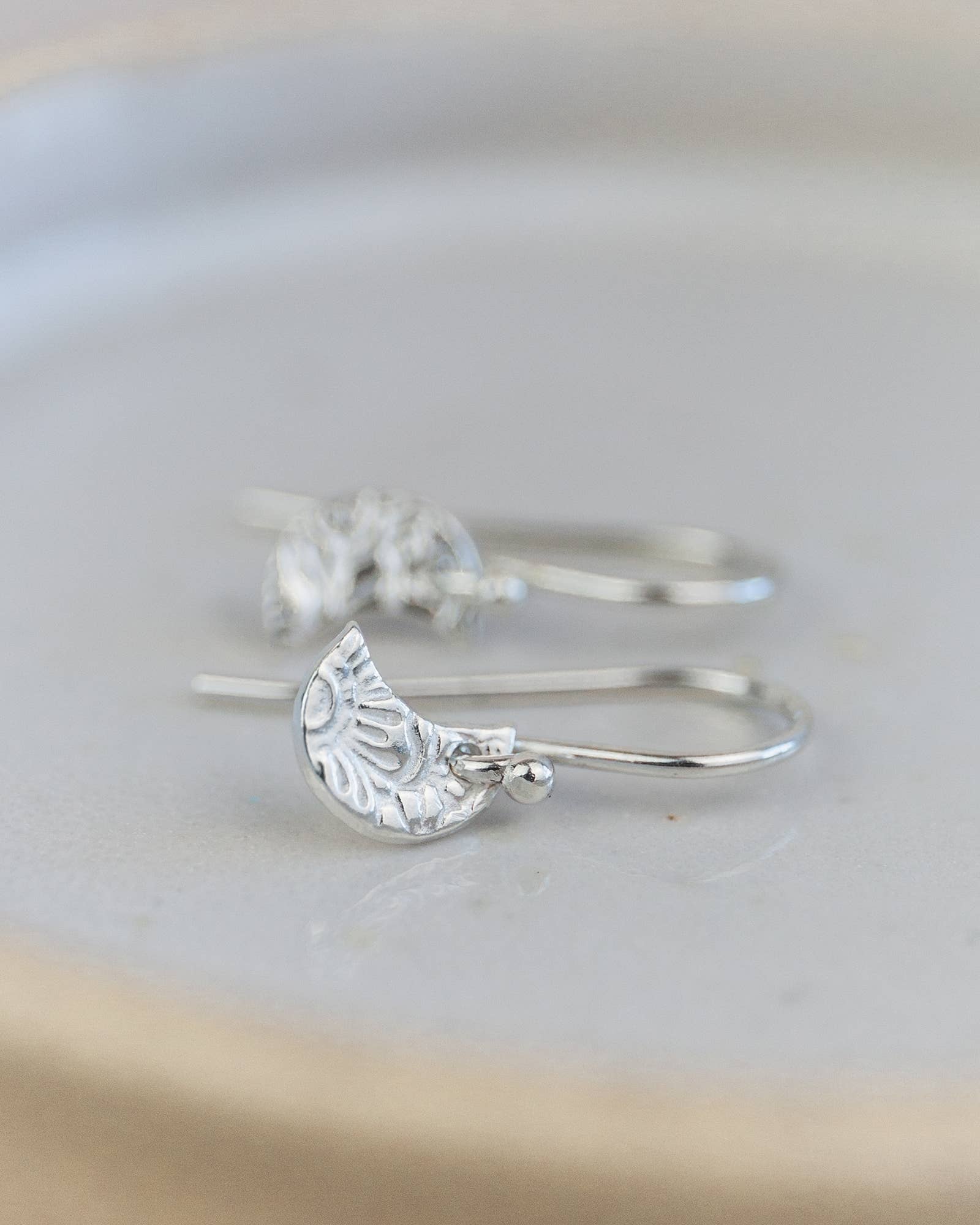 Silver earrings with half-circle designs on a light gray background