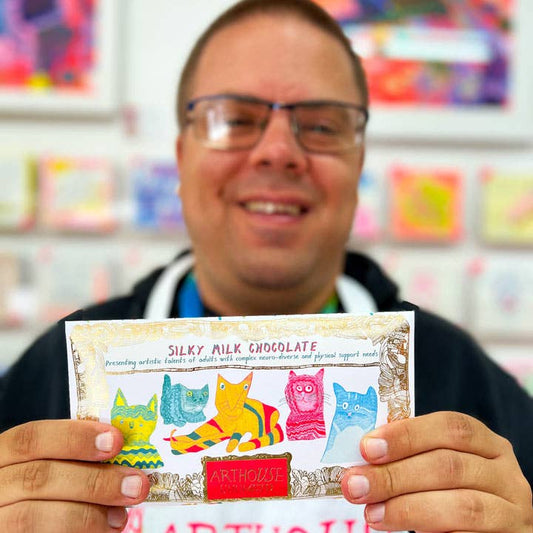Person holding a chocolate bar with colorful packaging featuring animals, against a blurred background of shelves with products.
