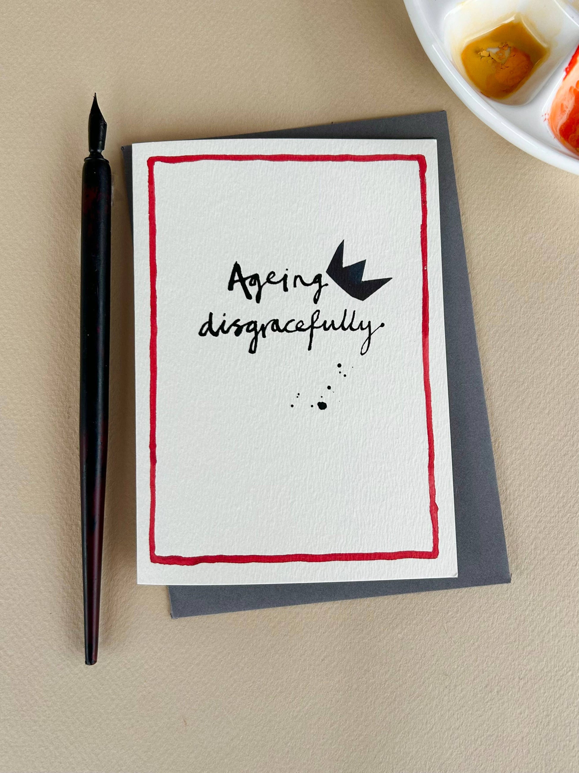 Ageing disgracefully in ink with a toppling crown on a cream card with red line around edge.