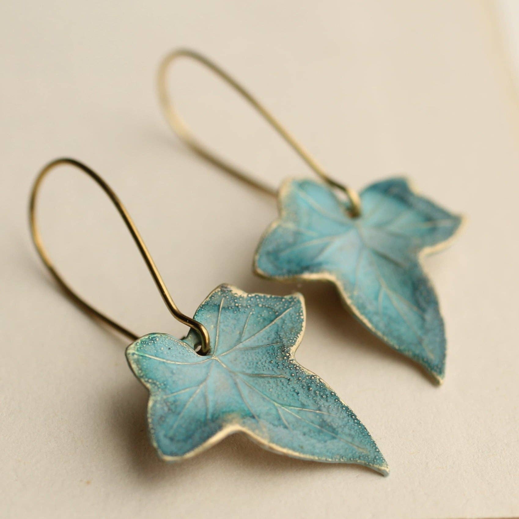 Pair of blue leaf-shaped earrings on a beige background