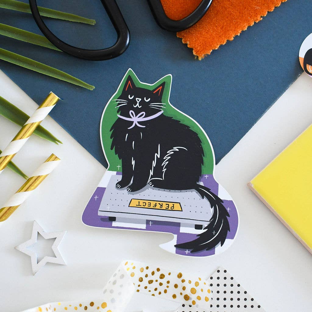 Sticker of a black cat on a laptop with office supplies in the background