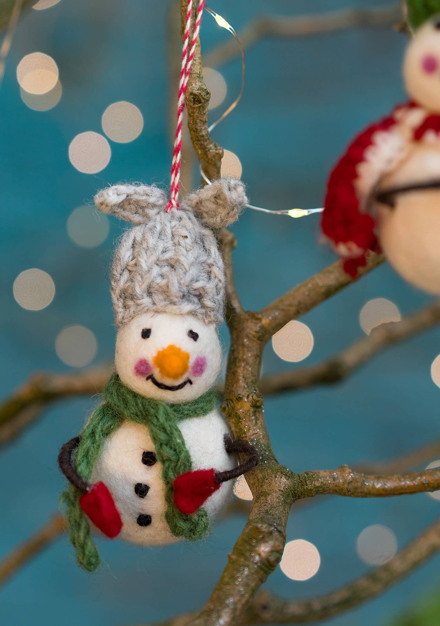 Felted snowman with colourful hat, scarf and bendy arms with mittens on.