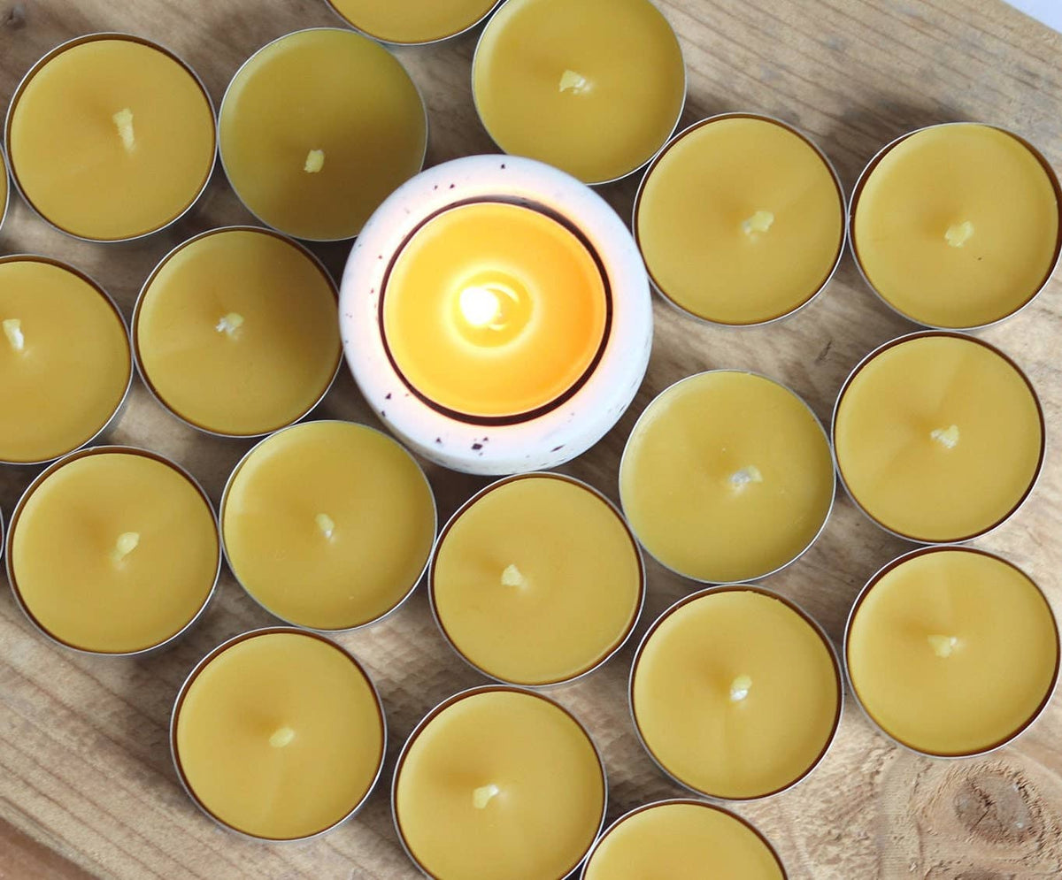 Yellow candles in metal containers with a lit candle in the center on a wooden surface