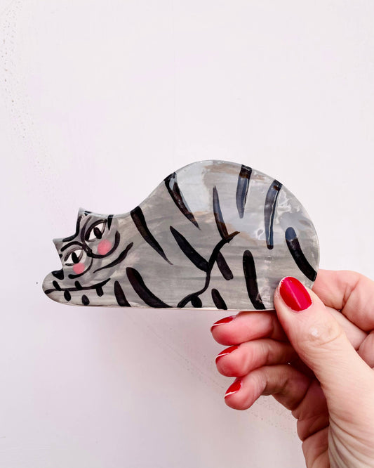 Hand holding a wooden cat-shaped object with zebra stripes on a white background